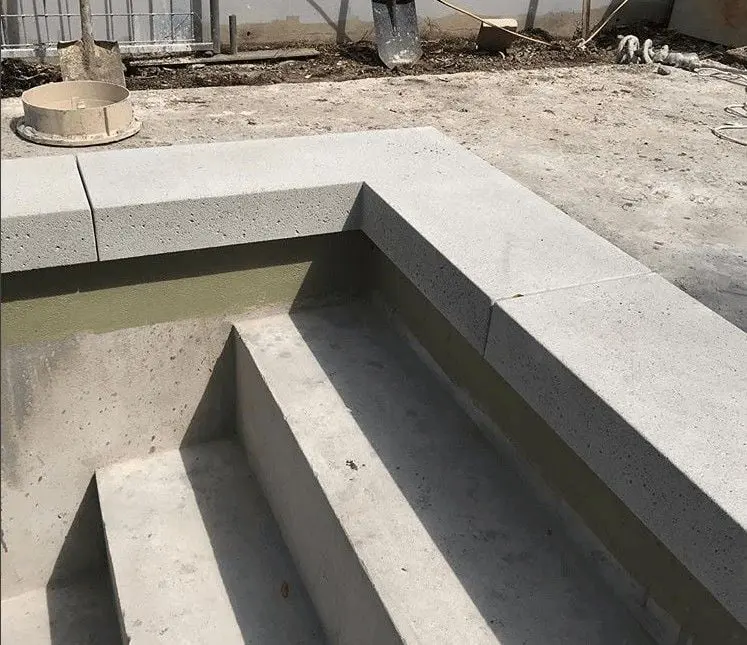 A concrete staircase leading into a partially constructed pool, with light gray steps and a matching ledge. Construction tools and debris are visible in the background, indicating an unfinished project. Skilled concrete contractors in Gardnerville NV can offer you a free quote to complete this area.