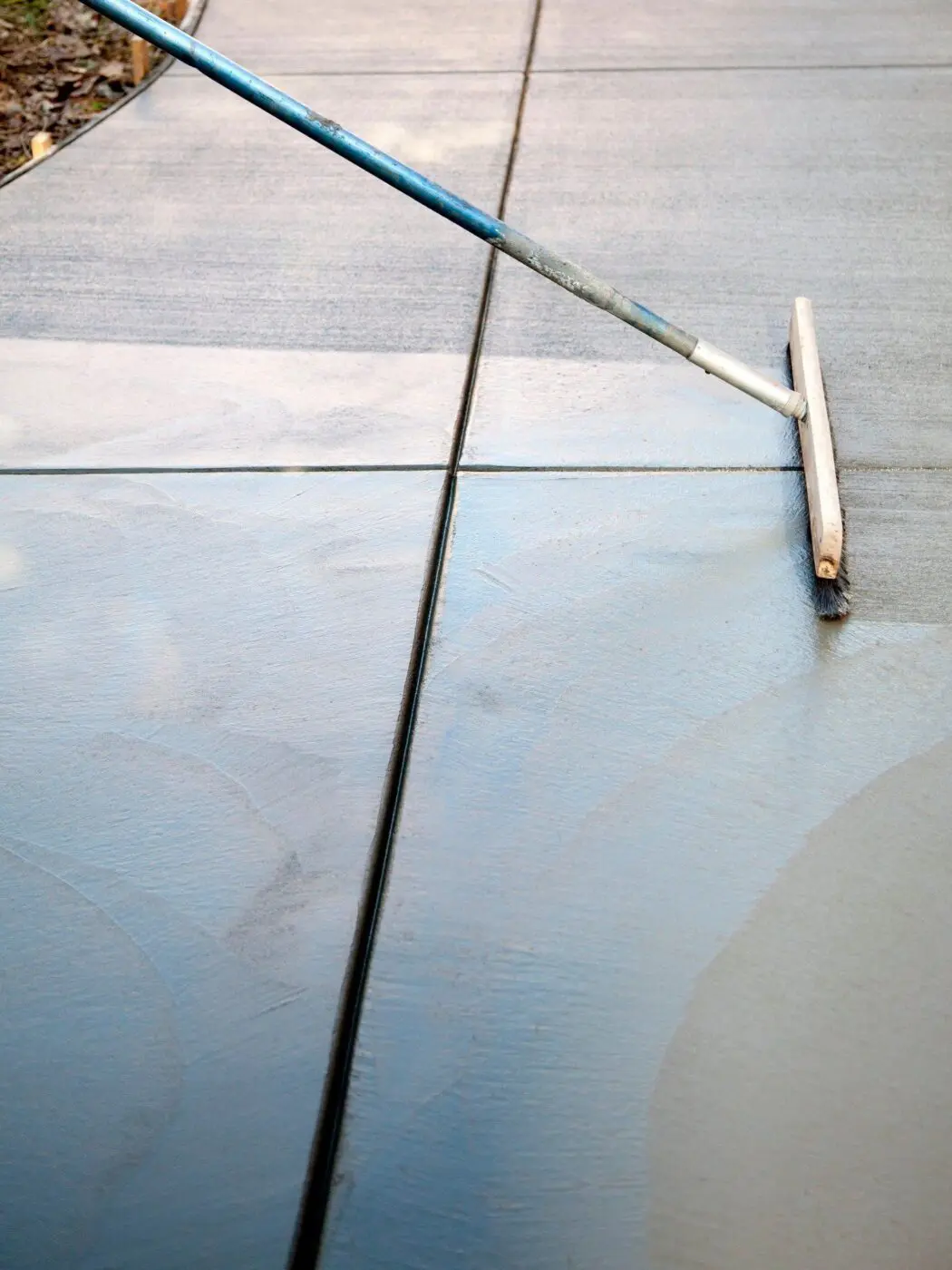 A close-up of a person using a concrete float tool to smooth and level freshly poured concrete on a sidewalk. The concrete is partially dried, and the float tool features a long handle and broad, flat head. The surface appears smooth and even. For expert services like this, contact Reno Concrete Solutions for a free quote.