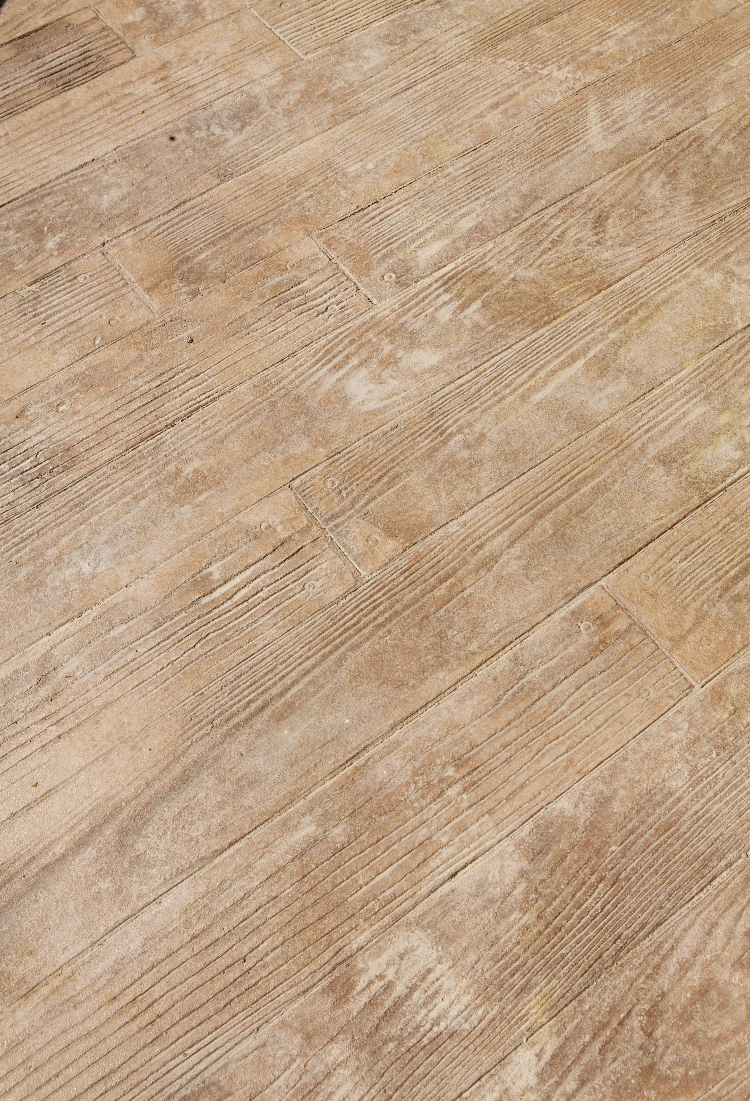 The image shows a close-up view of a wooden floor with a weathered, textured surface. The planks display a variety of natural wood grains and knots, with a slightly distressed and rustic appearance, giving the floor a vintage and well-worn look reminiscent of Sun Valley decorative concrete finishes.